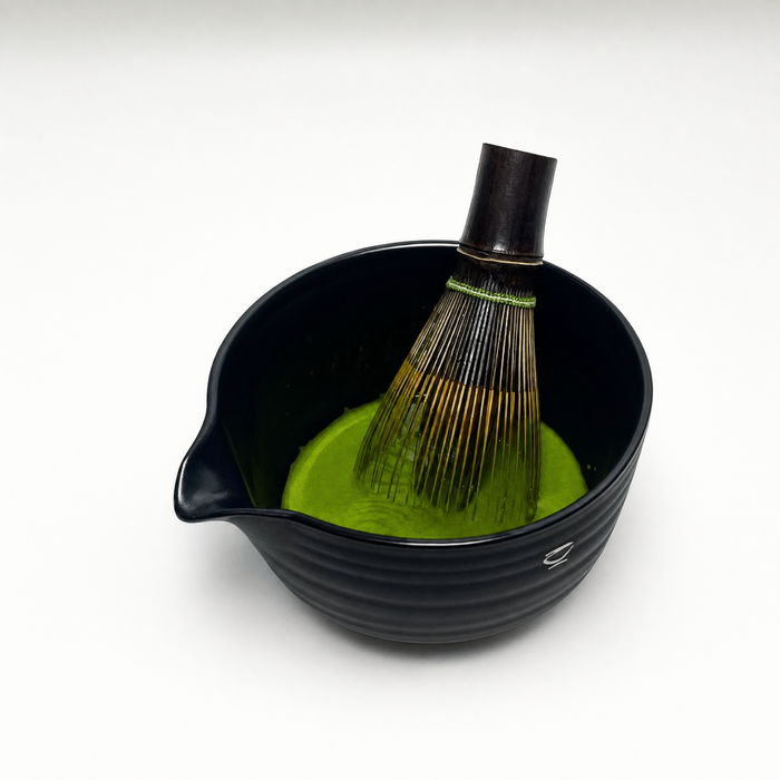 Bamboo whisk mid-motion in a bowl, splash frozen, warm light