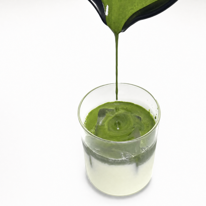 Oat milk pouring into green matcha, latte art swirl, ceramic cup